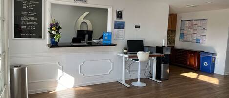 A hotel reception area with a desk, computer, and a large number '6' sign. There are signs for Continental Breakfast and a daily pet fee.