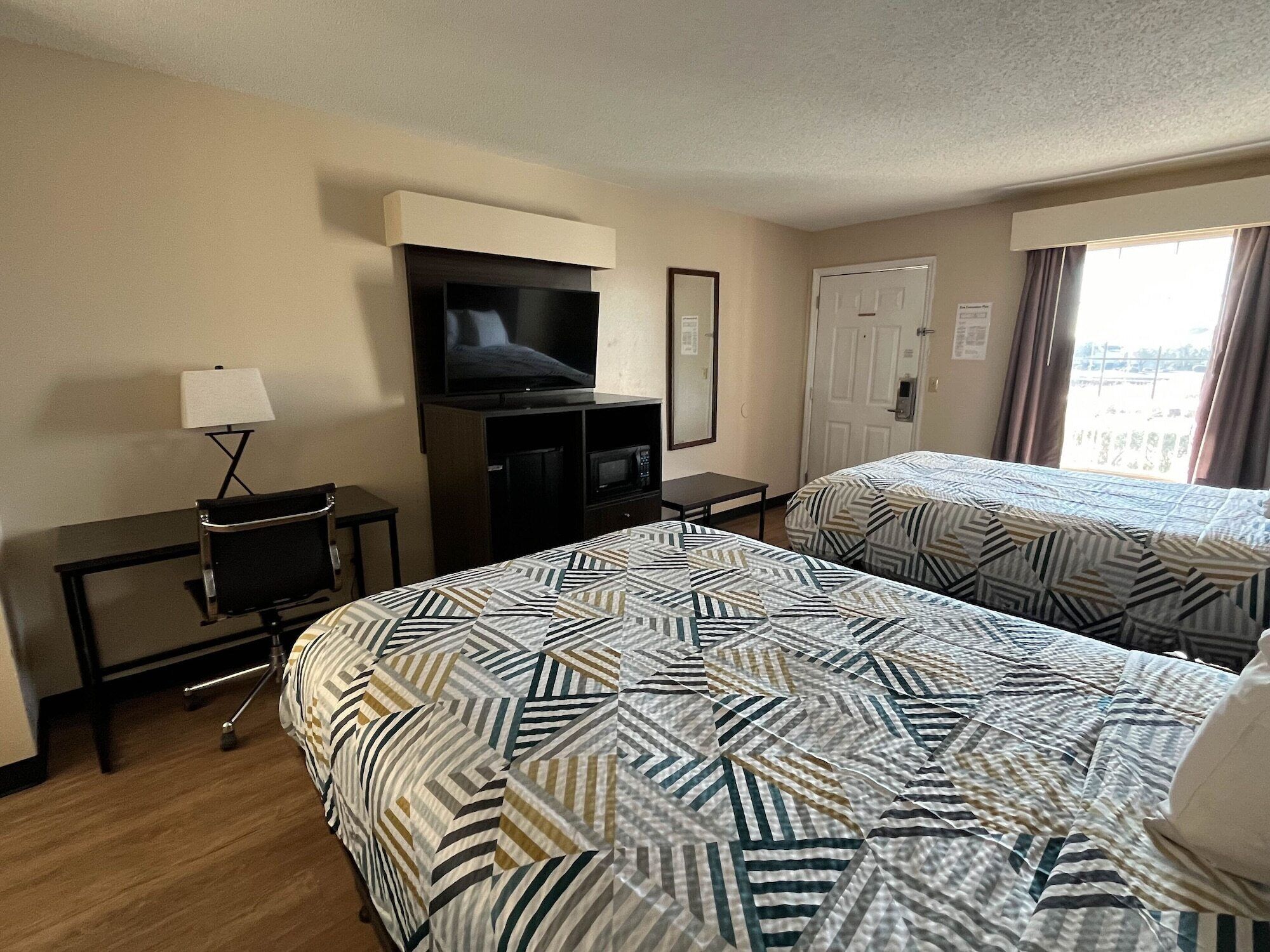 A hotel room with two beds, a TV, a desk, and a lamp.