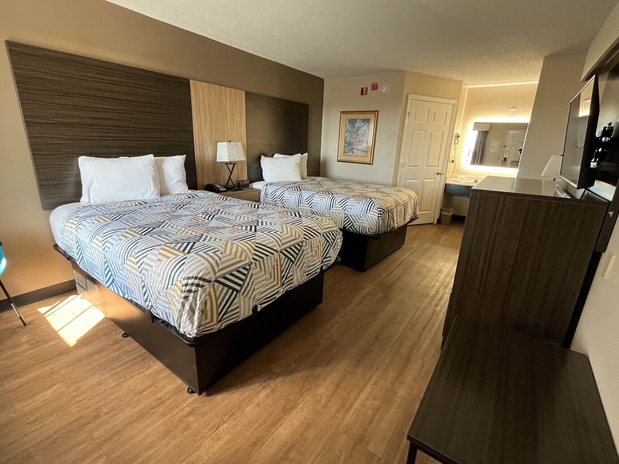 Habitación de hotel con dos camas, un escritorio, un espejo y una puerta que da al baño.