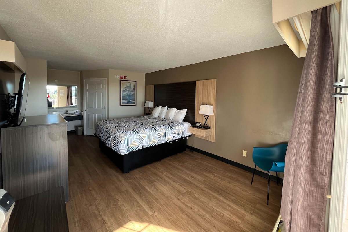 A hotel room with a bed, bedside table, lamp, and a chair.