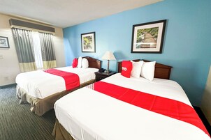 A hotel room with two beds, a nightstand, a lamp, and framed pictures on the wall.