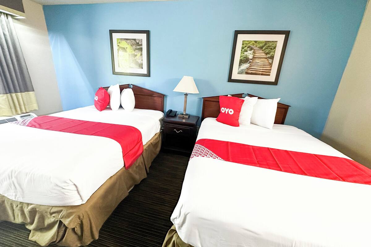 A hotel room with two beds, each with a red and white bedspread, a nightstand with a lamp, and framed pictures on the wall.