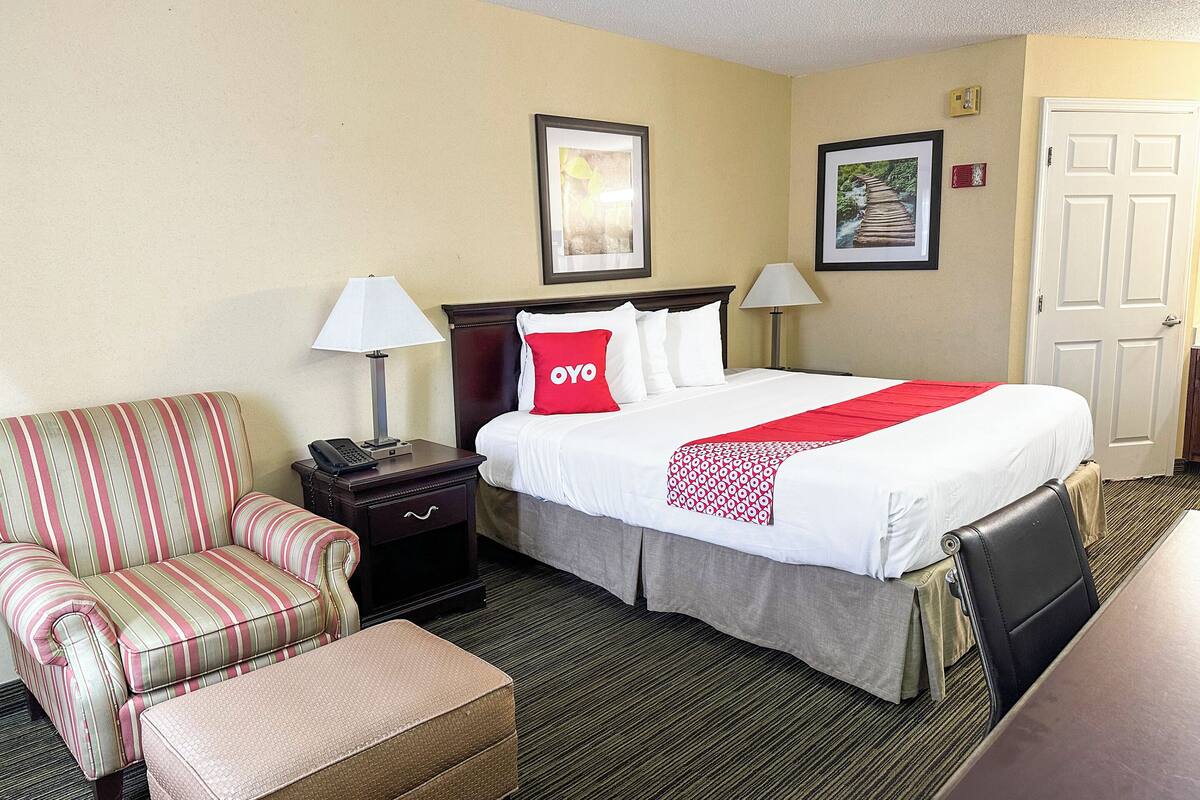 A hotel room with a bed, a striped armchair, a small table, and two bedside lamps.