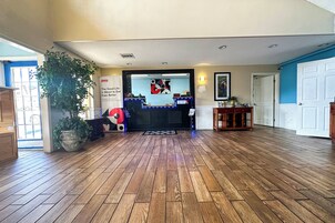 A spacious lobby with wooden flooring, a reception desk, and a large potted plant.