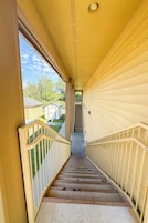 A staircase with a handrail leading to a landing, surrounded by yellow walls and a window overlooking a yard with a small building.