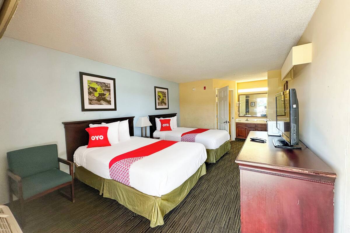 A hotel room with two beds, a desk, a chair, and a TV.