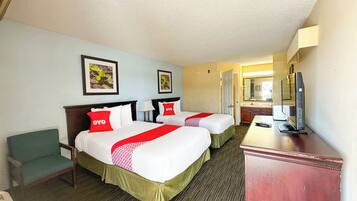 A hotel room with two beds, a desk, a chair, and a TV.