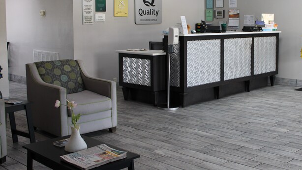 Zona de recepción con mostrador, una silla, máquina de café y una pared con el letrero 'Quality by Choice Hotels'.