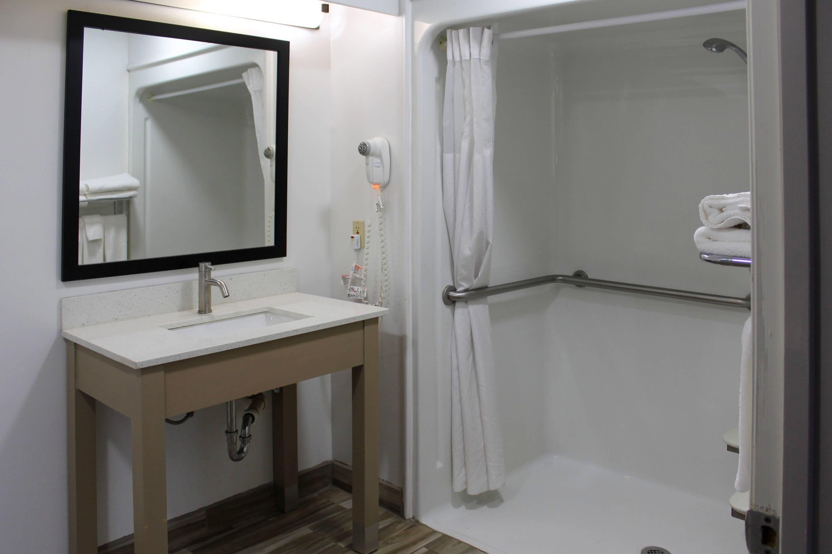 A bathroom with a sink, mirror, and shower.