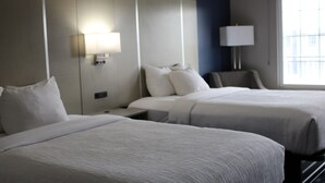 Habitación de hotel con dos camas, una mesita de noche, una lámpara y una ventana con vistas.