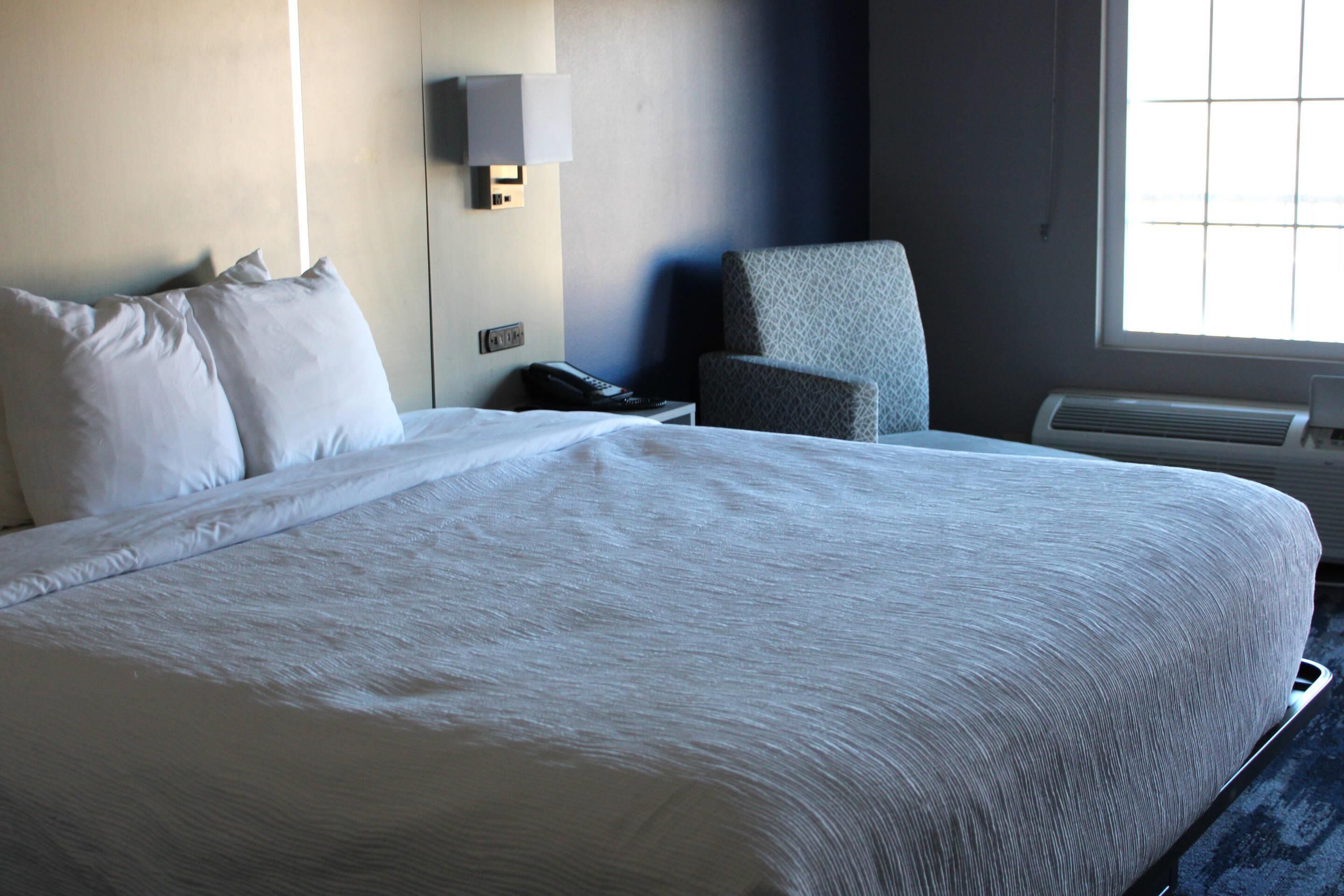 A hotel room with a large bed, a chair, a bedside table with a phone, and a wall-mounted lamp.