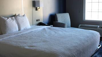 A hotel room with a large bed, a chair, a bedside table with a phone, and a wall-mounted lamp.