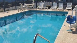 Una piscina con escalera metálica, sillas de descanso y solárium con baldosas.