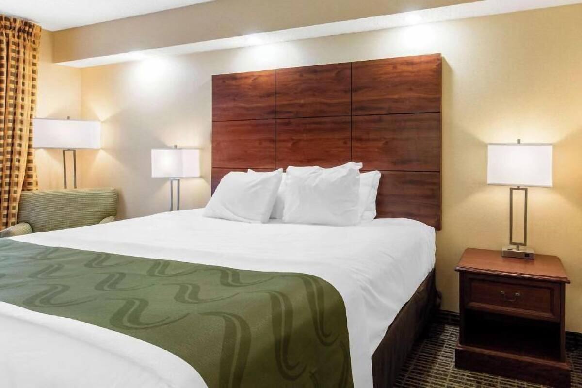 Ein Hotelzimmer mit einem großen Bett, zwei Nachttischlampen, einem Holz-Kopfteil und einer grün gemusterten Bettdecke.
