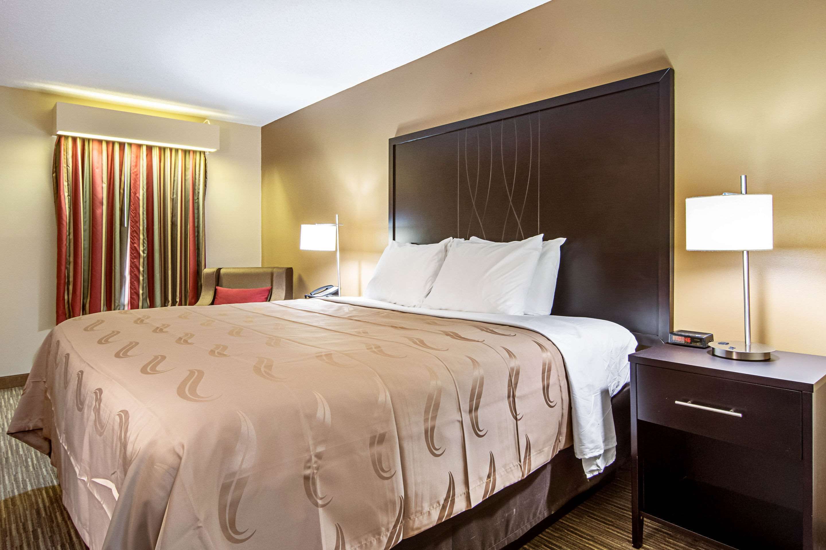 Une chambre d’hôtel avec un grand lit, une table de chevet avec une lampe, une chaise et un rideau.