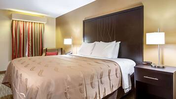 Une chambre d’hôtel avec un grand lit, une table de chevet avec une lampe, une chaise et un rideau.