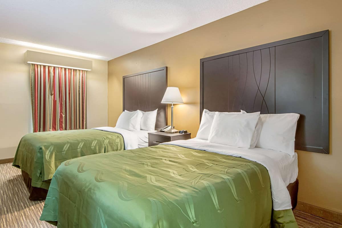 A hotel room with two beds, a nightstand, a lamp, and a striped curtain.