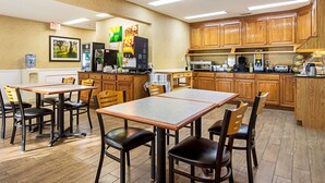 Una cocina de hotel con armarios de madera, una máquina de café, un microondas y un dispensador de agua.