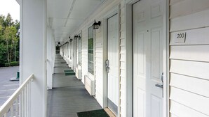 Un corredor techado con puertas blancas, numeradas 200, y un felpudo verde en la entrada.