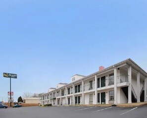 A multi-story motel with a row of rooms, a parking lot, and a sign indicating a nearby quality store. - Quality Inn Thomaston (Thomaston)