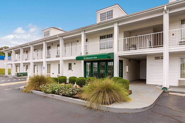 A two-story motel with a green awning labeled "Quality Inn," featuring a covered front porch and a landscaped entrance with shrubs and grasses. - Quality Inn Thomaston (Thomaston)