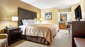 Una habitación de hotel con cama, mesita de noche, lámpara, escritorio con computadora y televisión.