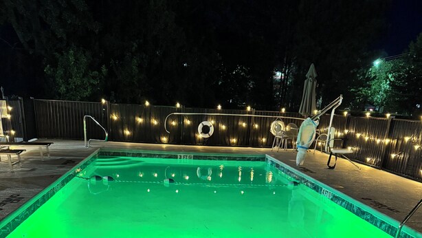 A swimming pool at night with green lighting, a lifebuoy, and a '5 FT NO DIVING' sign on the deck. - Baymont by Wyndham Thomasville (Thomasville)