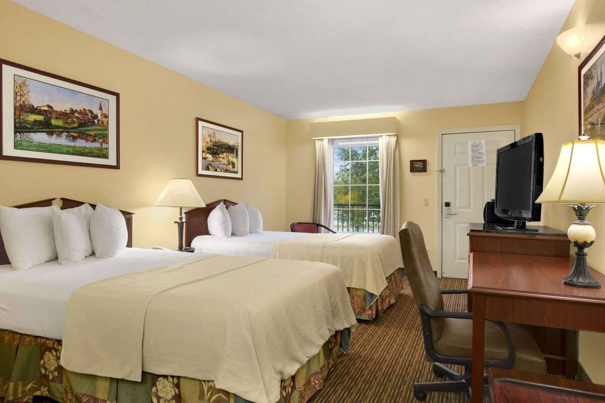 Habitación de hotel con dos camas, un escritorio, una silla, un televisor y dos cuadros en la pared.