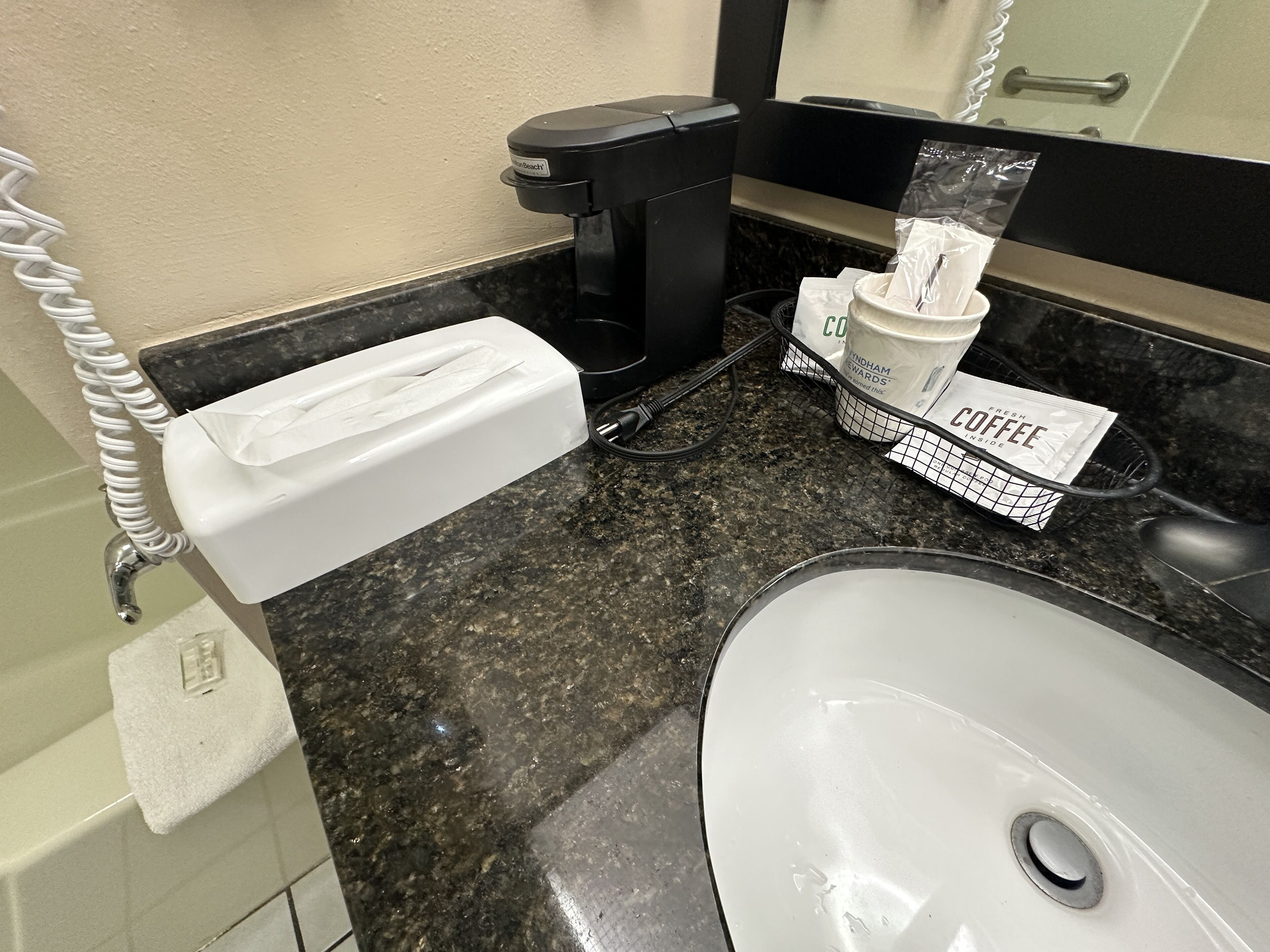 A bathroom with a white sink, a black coffee machine, a tissue box, and a coffee cup holder.