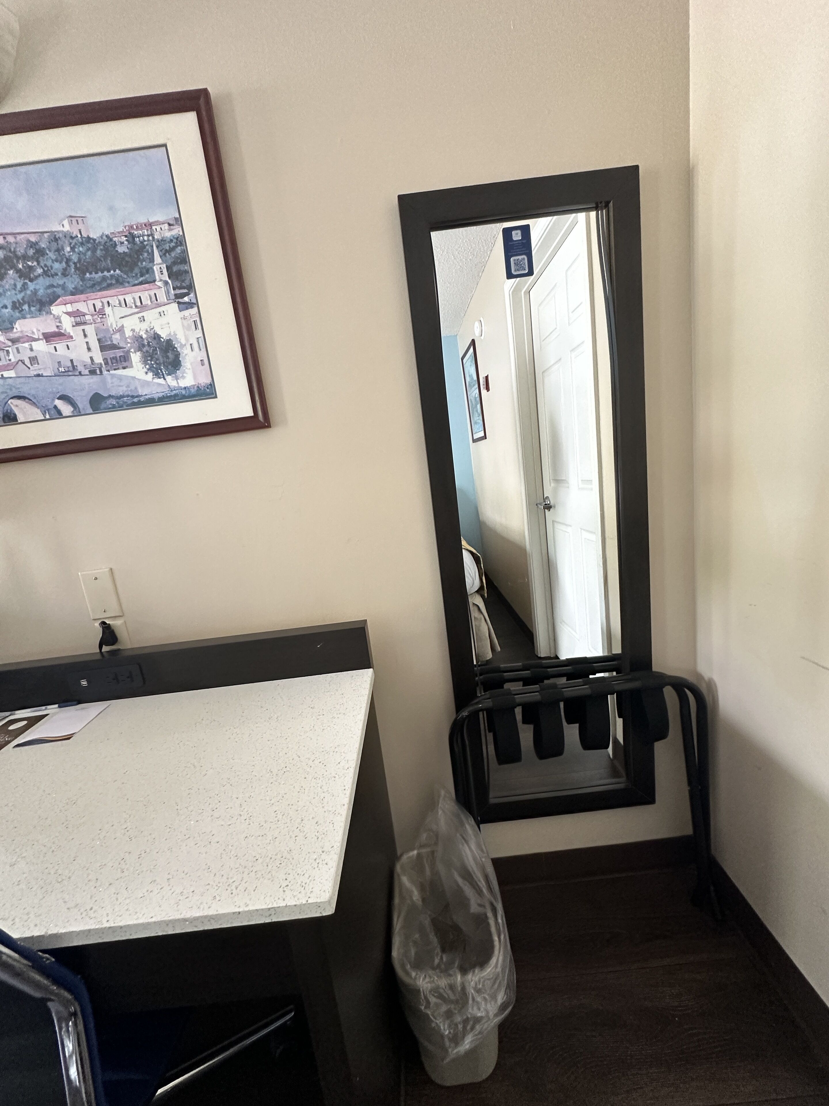 Una habitación de hotel con una cama, una mesita de noche, un cuadro enmarcado en la pared y un cubo de basura.
