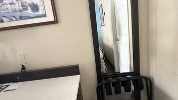 A hotel room with a bed, a bedside table, a framed picture on the wall, and a trash bin.