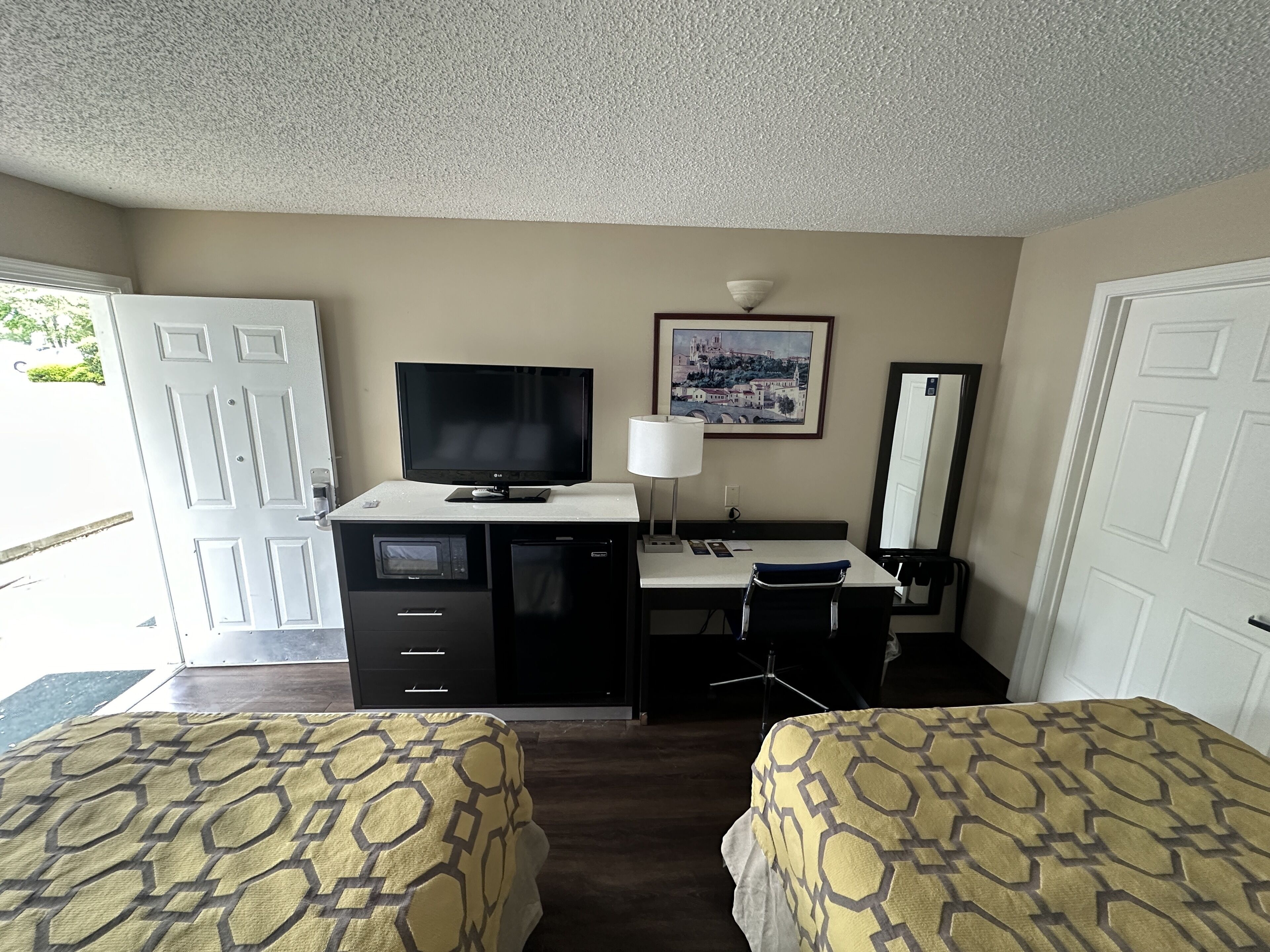 Habitación de hotel con dos camas, un escritorio, un televisor, un microondas, una lámpara y un cuadro en la pared.