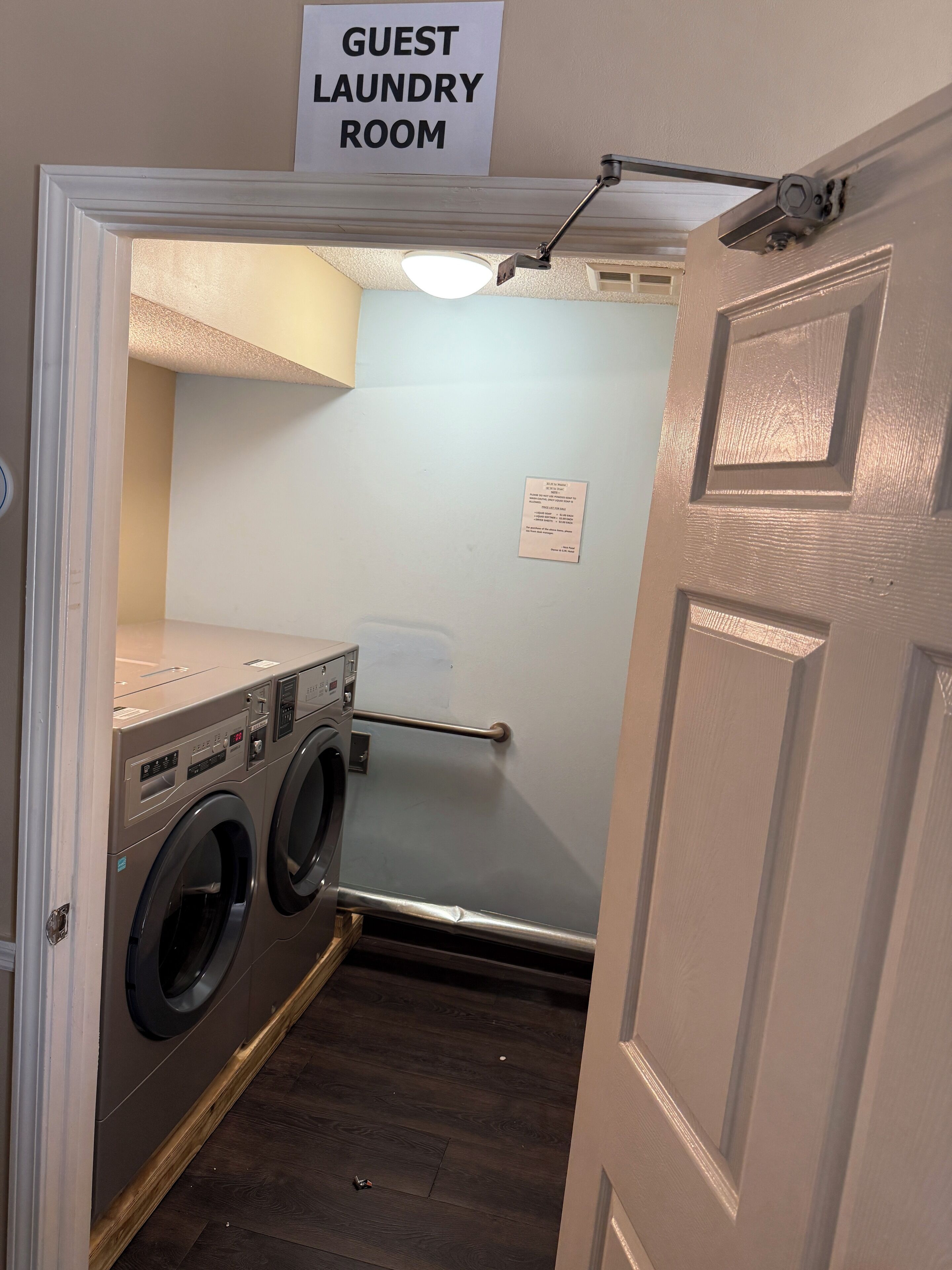 A guest laundry room with a washing machine, a dryer, a towel rack, and a sign indicating it's a guest area.