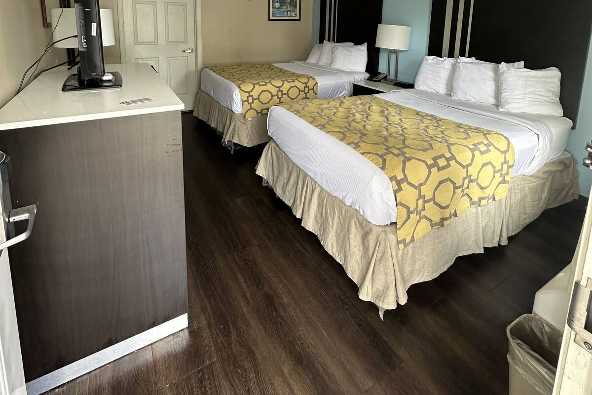 Una habitación de hotel con dos camas, un escritorio, un televisor y un cubo de basura.
