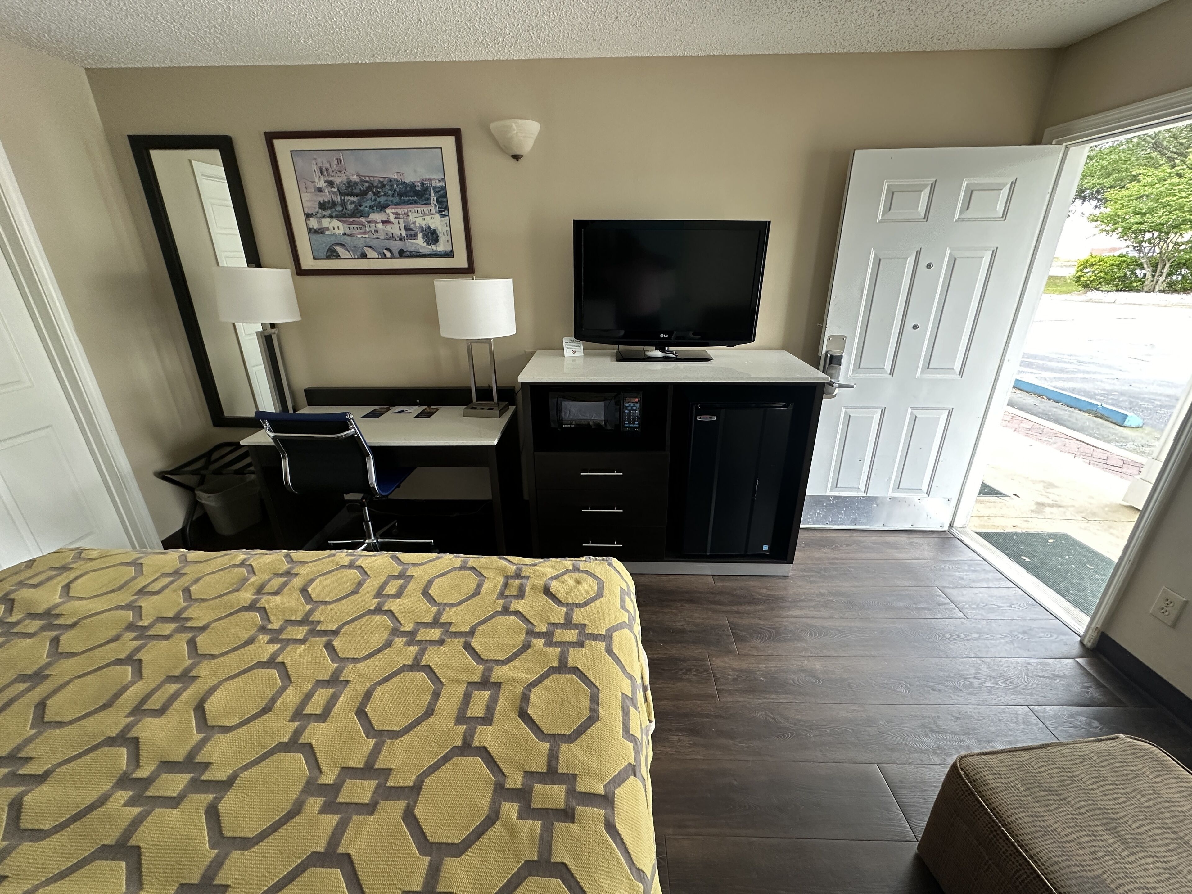 Habitación de hotel con cama, escritorio, televisor y puerta que da a un balcón.