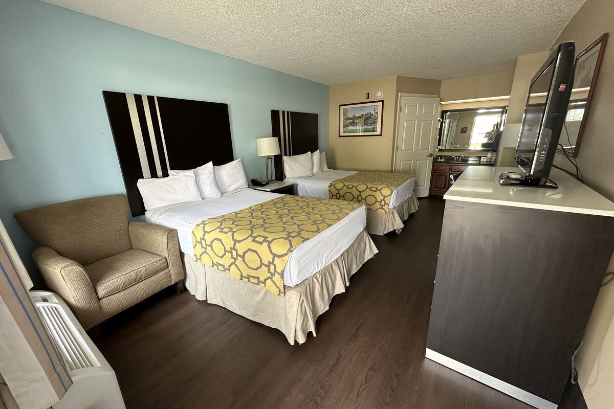 Habitación de hotel con dos camas, un sofá, un escritorio con computadora y un espejo.