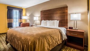 A hotel room with a large bed, two bedside lamps, a nightstand, and a wooden headboard. - Quality Inn Washington GA (Washington)