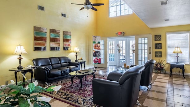 A spacious living room with a black leather sofa, a coffee table, and a ceiling fan. There are two lamps on side tables, a large rug, and a door leading outside. - Quality Inn Washington GA (Washington)