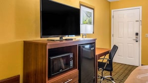 A hotel room with a wooden desk, a flat-screen TV, a microwave, a refrigerator, a black office chair, and a white door. - Quality Inn Washington GA (Washington)