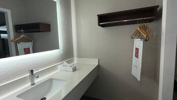 Un baño moderno con un lavamanos blanco, un espejo grande y un estante de madera con perchas.
