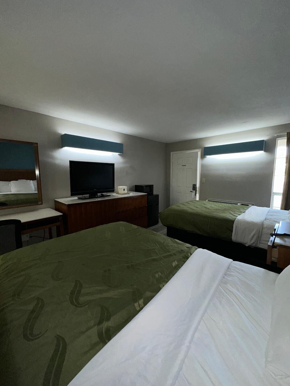 Une chambre d’hôtel avec deux lits, un bureau, une télévision et une porte.