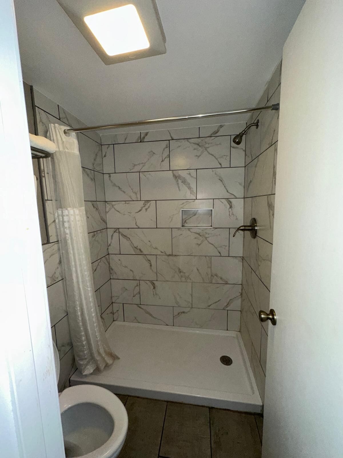 A bathroom with a shower, toilet, and a small window.