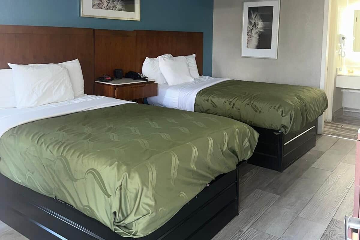A hotel room with two beds, a wooden headboard, a small table with a phone, and a framed picture on the wall.