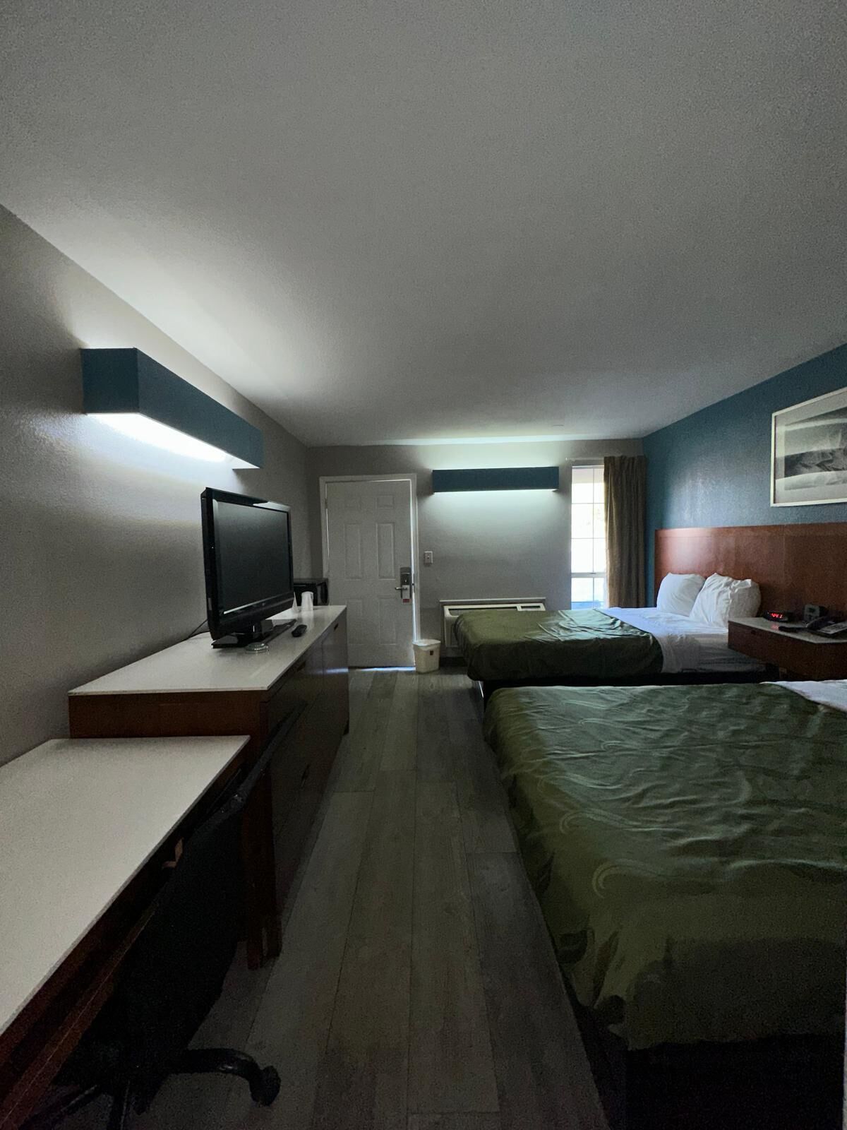Habitación de hotel con escritorio, televisor, dos camas y una ventana con cortinas.