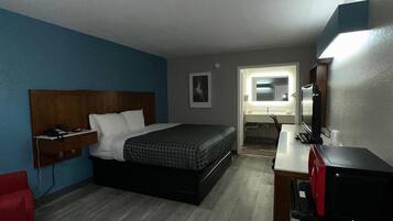 A bedroom with a bed, a desk, a chair, and a TV.