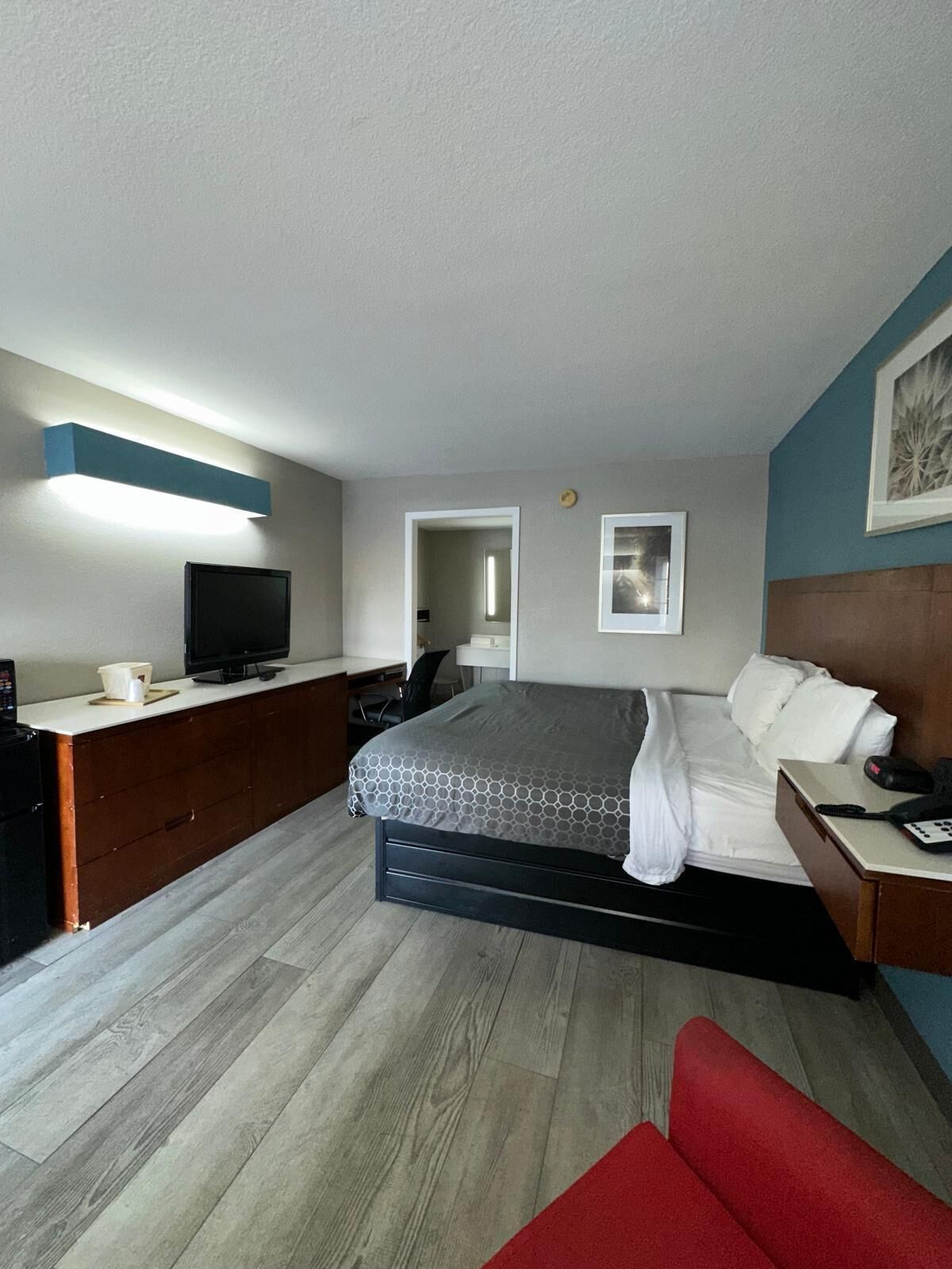 Habitación de hotel con cama, escritorio, televisor y una silla roja.