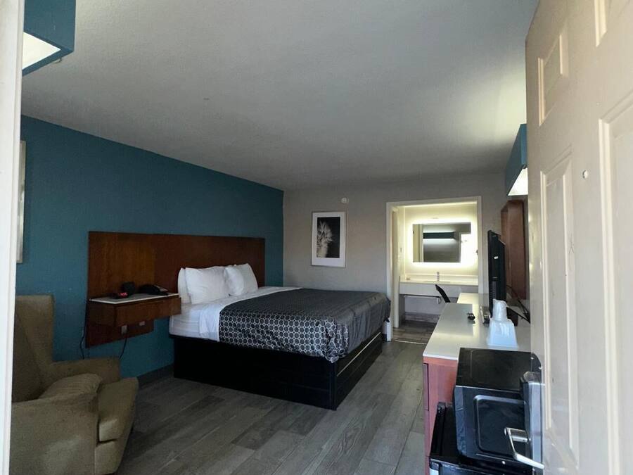 A compact hotel room with a bed, a desk, a chair, and a small kitchenette.