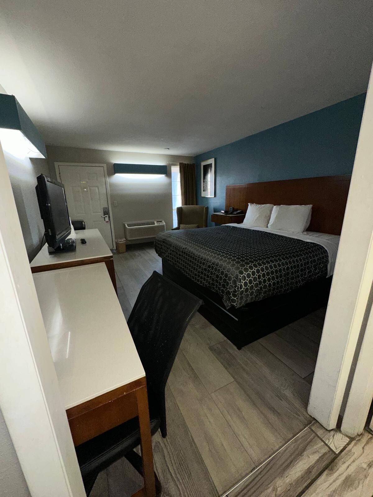 A compact hotel room with a bed, a desk, a chair, a TV, and a window.