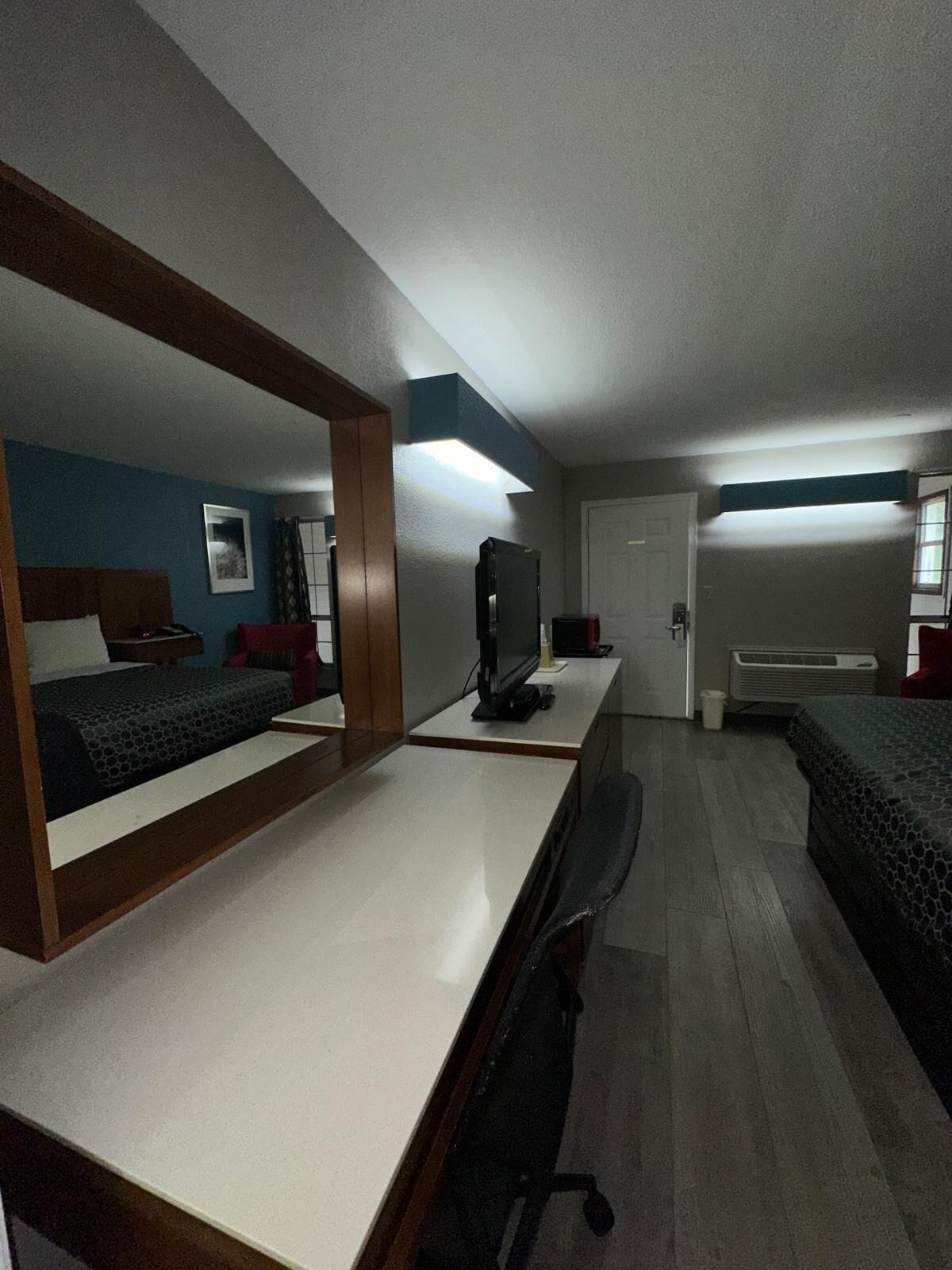 A compact hotel room with a single bed, a desk, a chair, a television, and a door.
