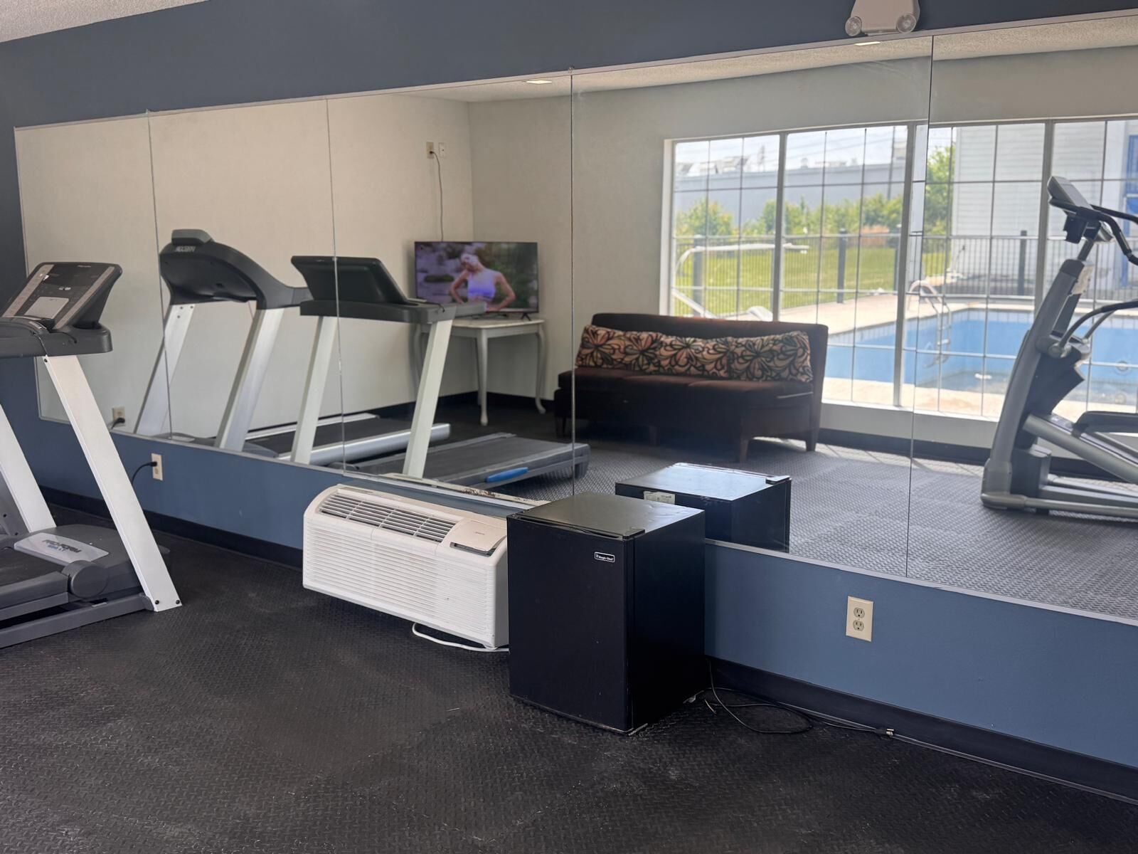 A gym with treadmills, a stationary bike, a treadmill, a sofa, and a large window with a view of a pool.